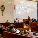 widok sali Sejmu z oddali, na ekranie wizerunki radnych biorących udział w sesji zdalnie