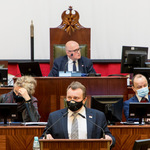 mężczyzna przemawia na mównicy w tle prezydium Sejmiku