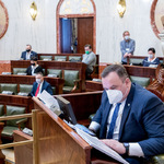 widok sali Sejmu z oddali - z przodu siedzący mężczyzna w oddali w ławach zasiadają radni