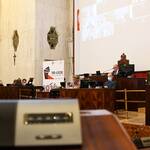 widok sali Sejmu z oddali: na ekranie widoczni radni biorący udział w sesji zdlanie, w oddali Prezydium Sejmiku oraz przedstawiciele Zarządu Województwa