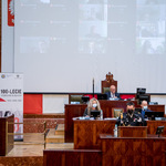 mężczyzna przemawia z mównicy, w tle Predyzium Sejmiku, na ekranie radni biorący udział w sesji zdalnie