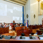 widok sali Sejmu z oddali, prezydium, występujący zespół, goście, na ekranie radni biorący udział w sesji zdalnie