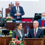 widoczne prezydium Sejmiku - osoby w postawie stojącej, przy mównicy śpiewają kobieta i mężczyzna