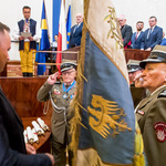 sala Sejmu zapełniona gośćmi, na pierwszym planie mężczyzna w mundurze przekazuje duży sztandar drugiemu mężczyźnie