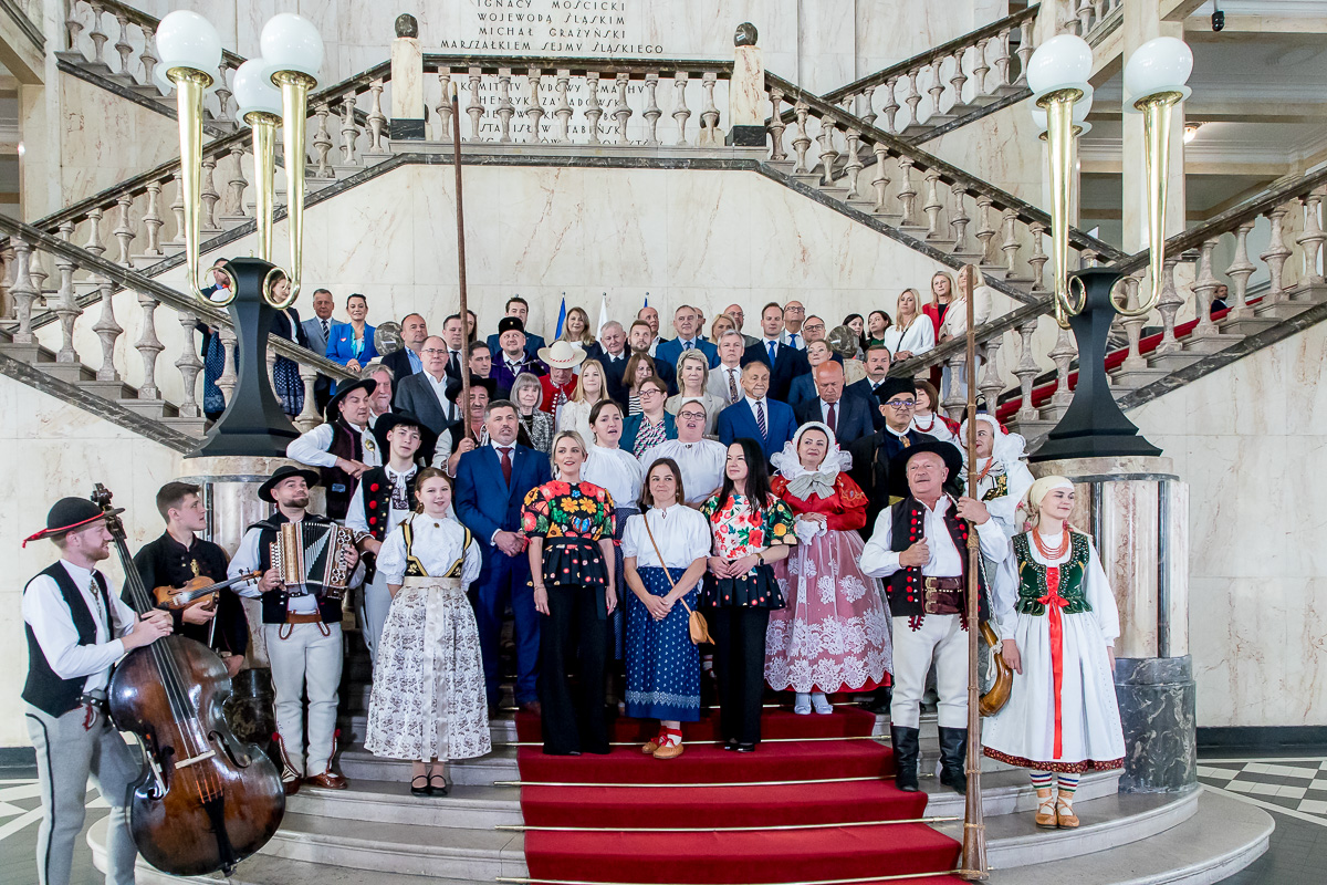 zdjęcie z oddali - tłum ludzi - radni, osoby w strojach ludowych - stoi na okazałych schodach na westybulu budynku urzędu
