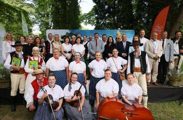 kilkudziesięcioro ludzi w postawie stojącej, wśród nich osoby w strojach góraskich