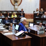 kobieta przemawia na mównicy w tle w ławach zasiadają ludzie