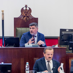 mężczyzna siedzący za biurkiem pracuje, poniżej siedzą trzy osoby