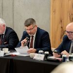 Mężczyzna siedzący za biurkiem przemawia do mikrofonu.